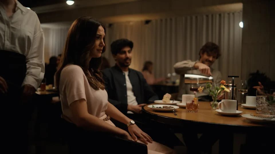 Frame from the Brex Spend Smarter, Move Faster film: a woman in a pale pink top seated at a busy restaurant table