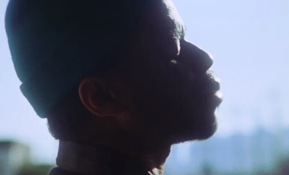 Frame from the Ovrkast. Outro music video: side profile of a man in a beanie, backlit against a pale blue sky