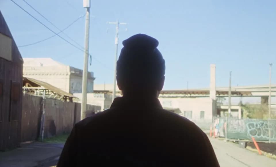 Frame from the Ovrkast. Outro music video: silhouette of a person in a beanie from behind on a sunny street
