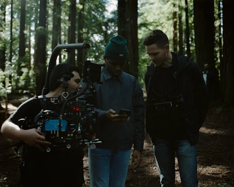 Behind the scenes on the Ovrkast. Outro shoot: Skyler, a camera operator, and a man in a green beanie checking a phone in a forest