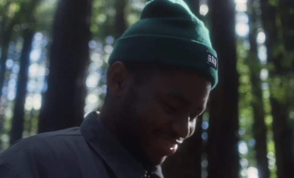 Frame from the Ovrkast. Outro music video: a smiling man in a green beanie looking down in a redwood forest