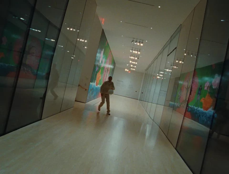 Woman running with a basketball down a long museum gallery lined with green and orange floral murals and mirrored walls
