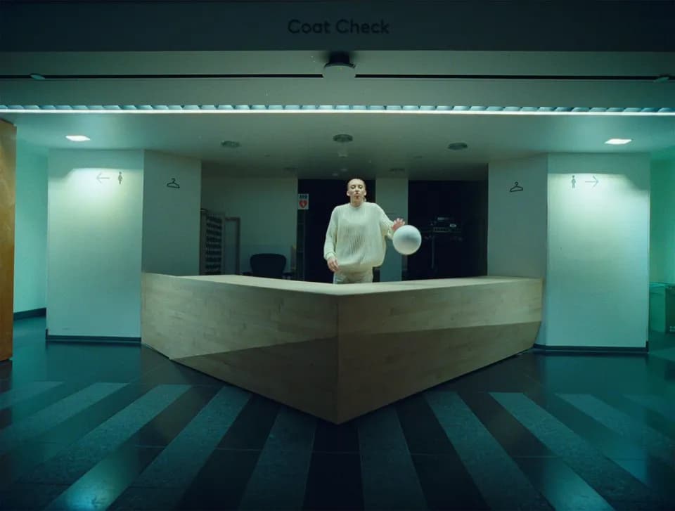Woman with a white basketball under a Coat Check sign behind a wooden counter in a dim museum lobby