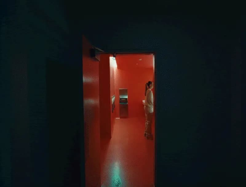 Cash Studios x SFMoMA spot: a woman in a pale outfit stands in a doorway at the end of a dark hall, a red room beyond