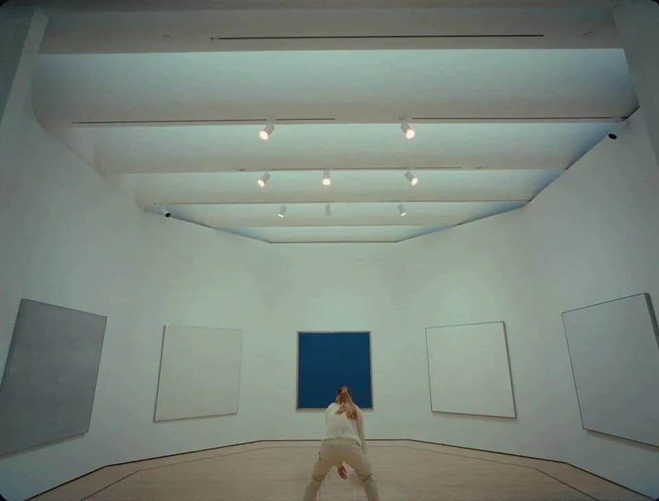 Frame from the SFMoMA Get in the Game film: woman crouched in a white gallery facing a blue canvas