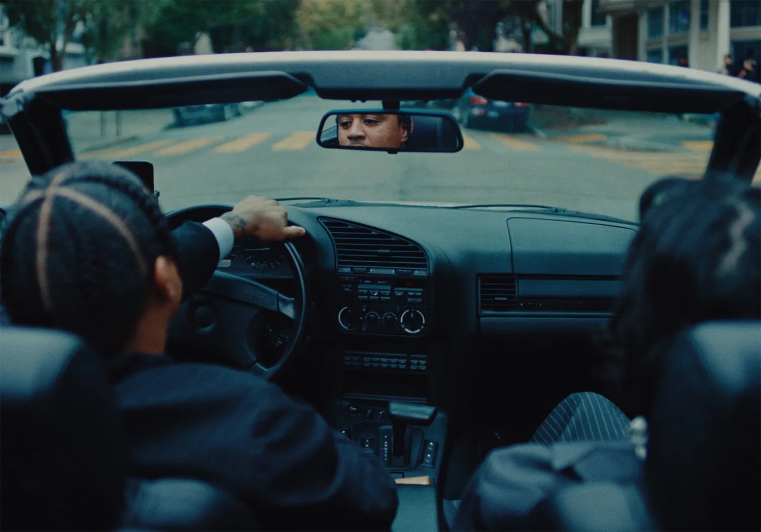 View from the back seat of a convertible: a driver's hand on the wheel and his face in the rear-view mirror