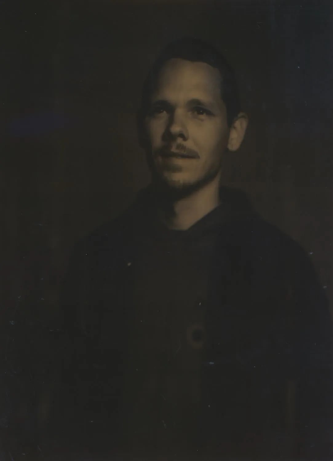 Portrait of Skyler Vander Molen: dark, sepia-toned film portrait of a man with a goatee in a dark hoodie and jacket