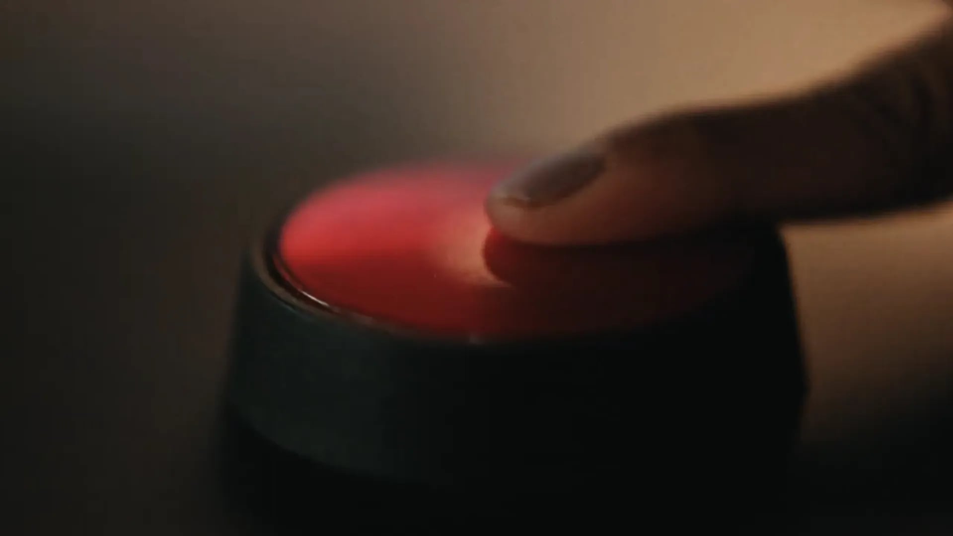 Finger pressing a glowing red button in a dark, warm-lit room