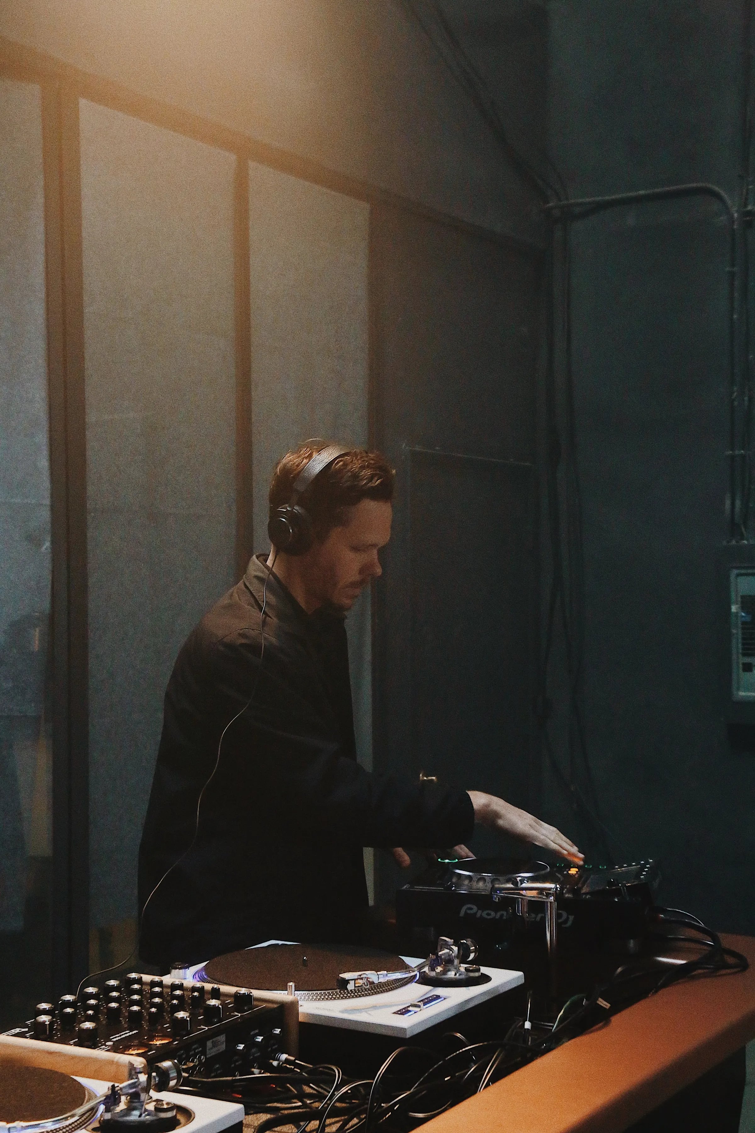 Skyler DJing wearing headphones using turntables and Pioneer DJ gear in a dim, blue-grey room