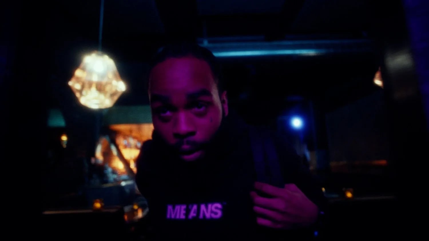 Frame from the Fly Anakin No Dough music video: man in a hoodie lit purple, a chandelier glowing behind him