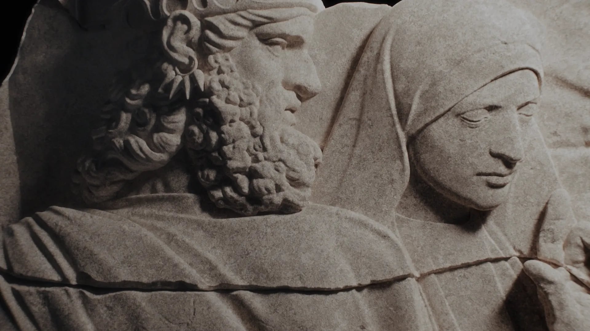 Close-up of a carved stone relief with a bearded man in profile beside a veiled woman looking down, from the Forum identity