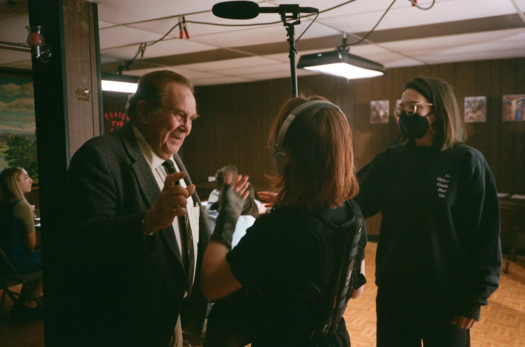 Behind the scenes of No Other Gods But Me: an older man in a suit talks with a sound operator and a masked crew member