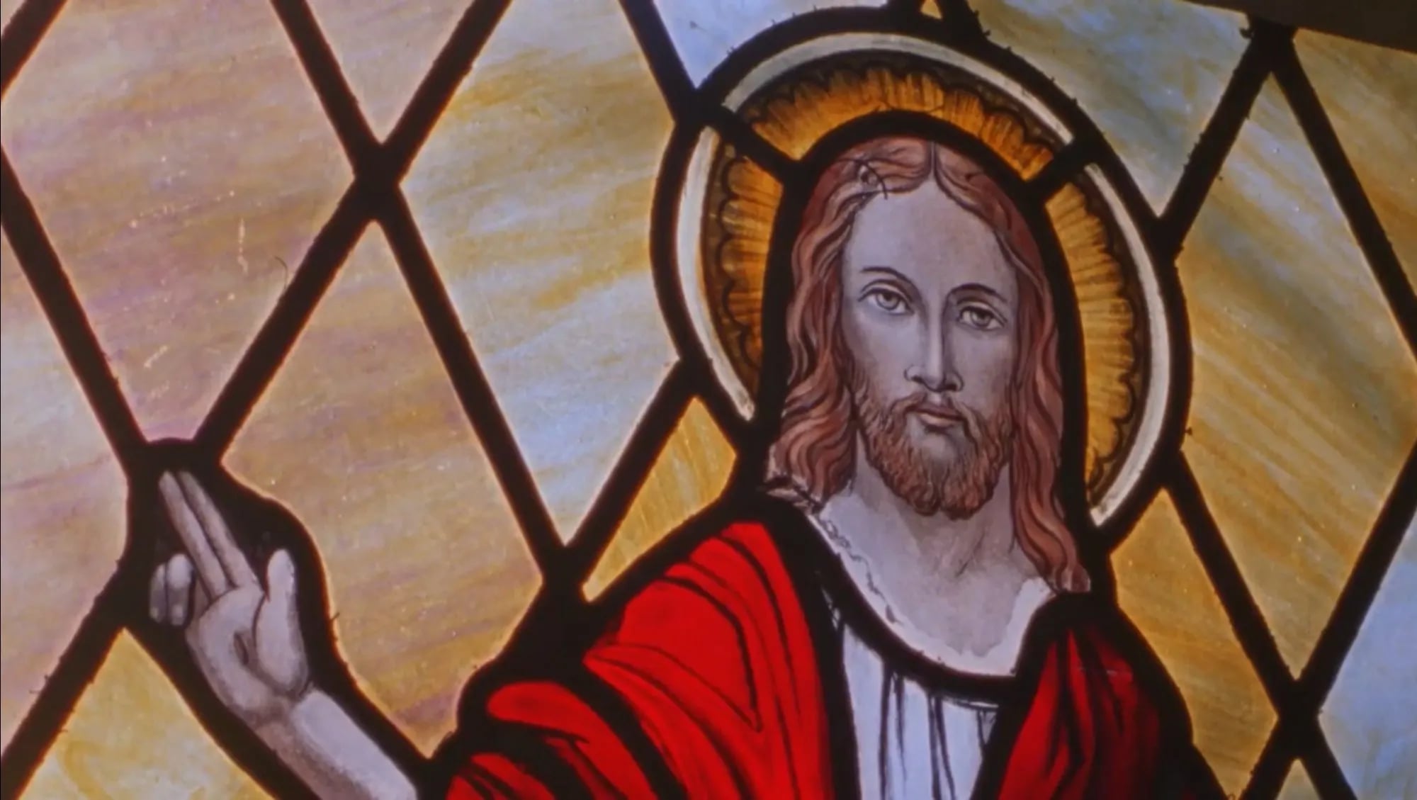 Film frame: a stained-glass window of Jesus in a red robe with a halo, raising a hand