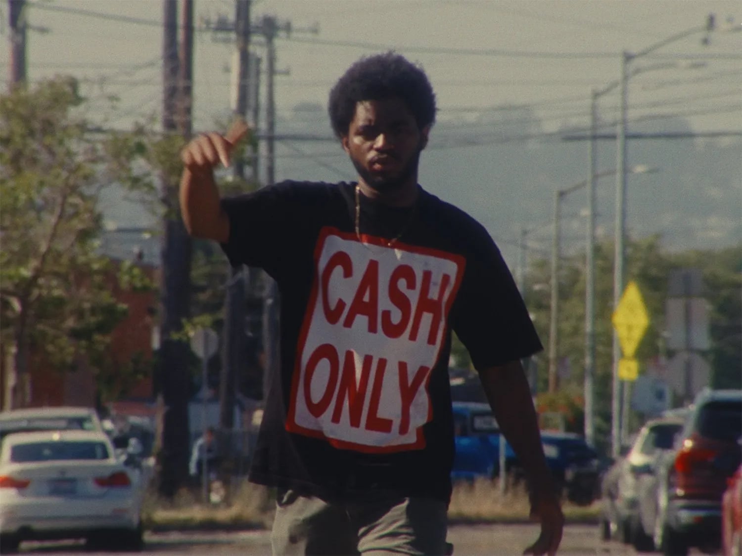 Frame from the Ovrkast. Bipper's Joint music video: a man in a black "CASH ONLY" tee walking down a street, one arm raised