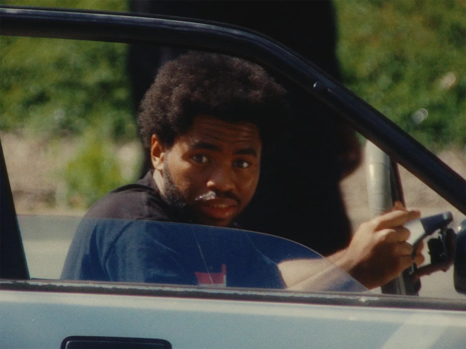 Frame from the Ovrkast. Bipper's Joint music video: a man with an afro looking back at the camera through an open car door