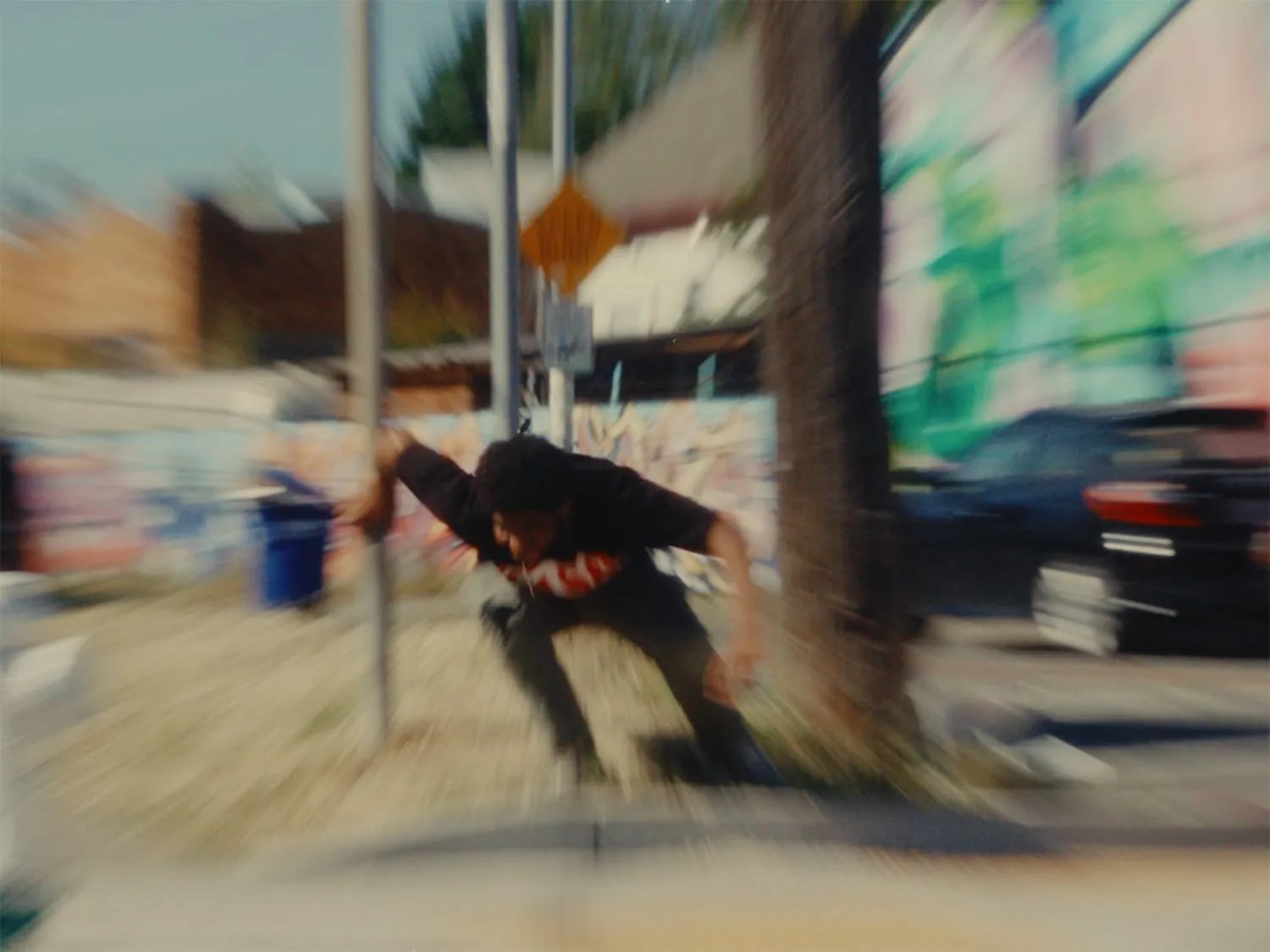 Blurred frame from Bipper's Joint of a man in motion beside a street pole, with graffiti and a dark car behind him