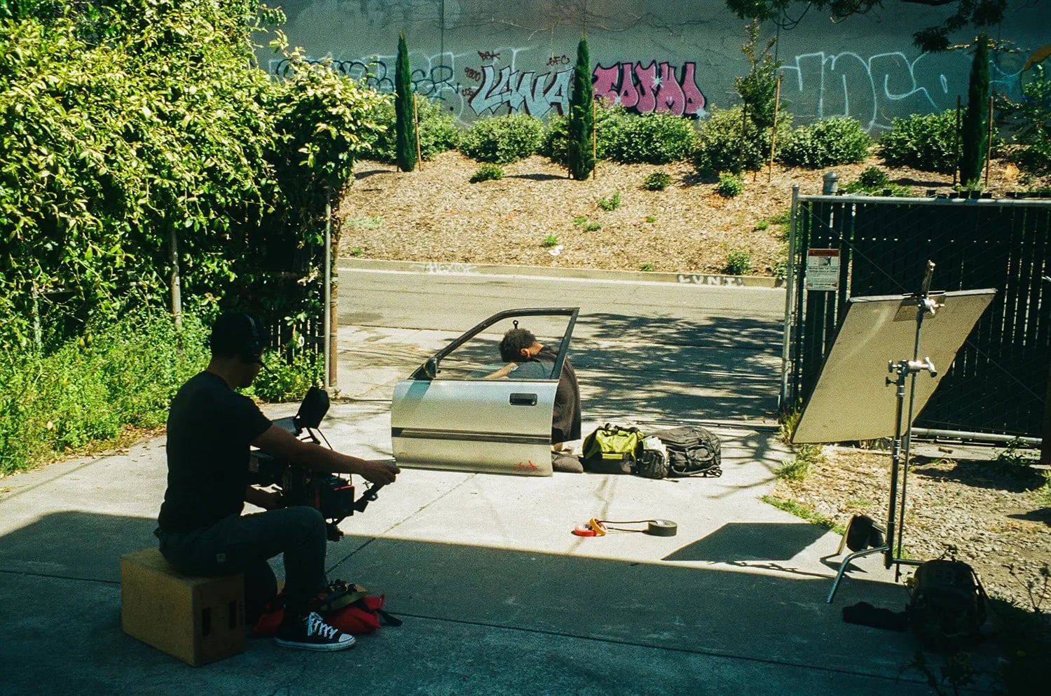Behind the scenes on the Bipper's Joint shoot: a camera operator seated on a box films a man sitting in an open car door