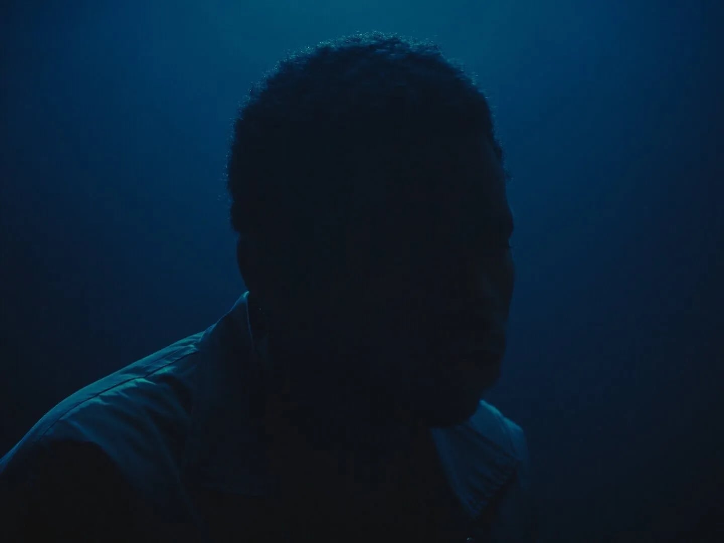 Backlit blue silhouette of a man's head and shoulders against a deep blue background