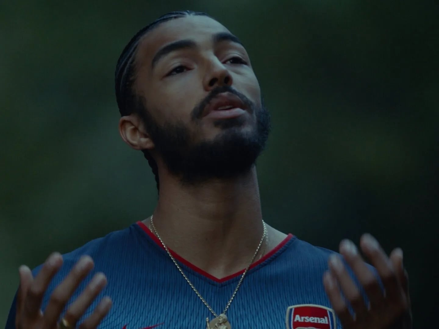 Frame from the Ovrkast. Face music video: man in an Arsenal football shirt and gold chain with open hands