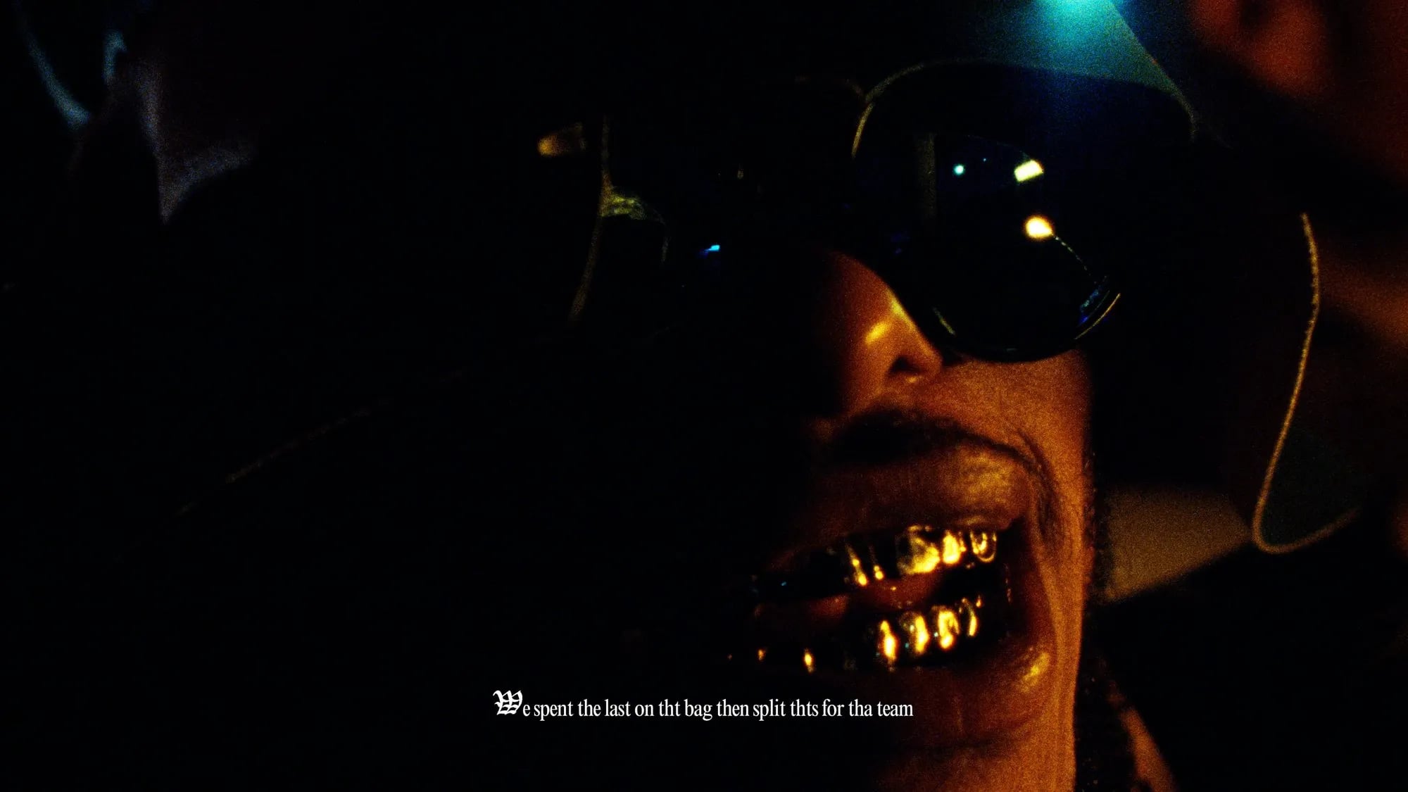 Frame from the Pink Siifu Fk U Mean / Hold Me Dwn music video: gold grill and sunglasses in dark light, lyric subtitle