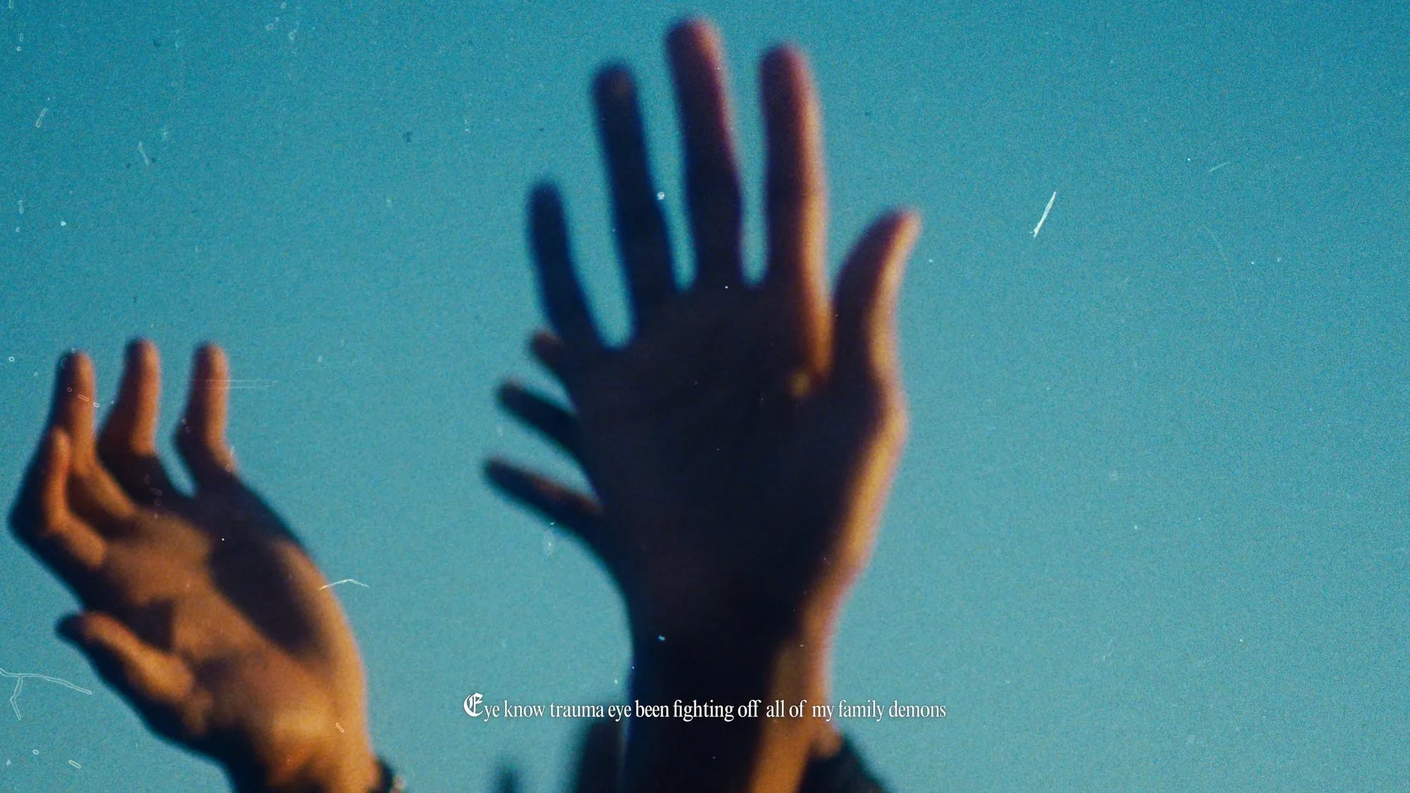 Two raised hands against a blue sky with film grain, subtitle "Eye know trauma eye been fighting off all of my family demons"