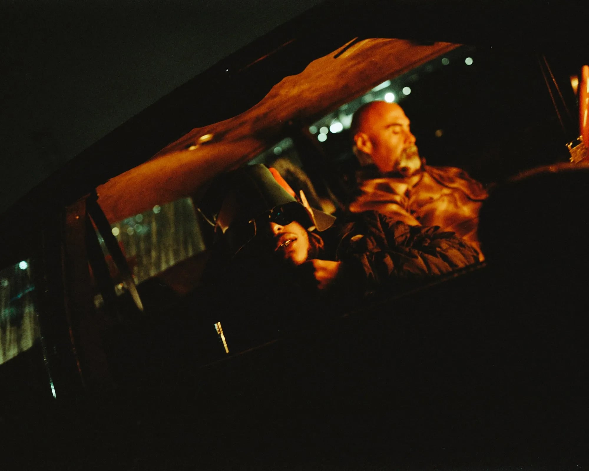 Behind the scenes, Pink Siifu shoot: two men seen through a car window at night, lit in orange, one in sunglasses